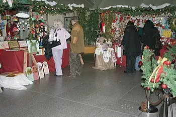 Ein Weihnachtsmarkt mit dekorativen Ständen, die mit festlichen Produkten geschmückt sind. Menschen sehen sich die Angebote an, während Weihnachtsdekoration die Umgebung ziert. Die Atmosphäre ist gemütlich und einladend.