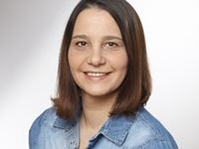 Tanja Unglaub Ein Porträt einer Frau mit mittellangen, braunen Haaren. Sie trägt ein denimfarbenes Hemd und lächelt freundlich in die Kamera. Der Hintergrund ist hell und neutral gestaltet.