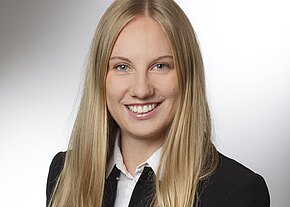 Porträtfoto: Eine lächelnde Frau mit langen blonden Haaren blickt in die Kamera. Sie trägt einen schwarzen Blazer über weißem Hemd. Neutraler, heller Hintergrund; klassisches Bewerbungs- oder Businessfoto.