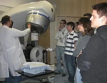 Ein Arzt in einem Laborkittel erklärt eine medizinische Maschine vor einer Gruppe interessierter Personen. Die Atmosphäre wirkt lehrreich, und die Zuhörer zeigen Neugier und Aufmerksamkeit für die Demonstration der Technologie.