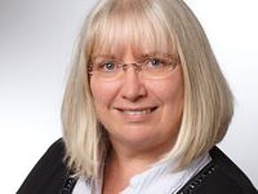 Petra Stolper Porträt einer Frau mit blonden, schulterlangen Haaren und Brille. Sie trägt eine schwarze Jacke und lächelt freundlich in die Kamera. Der Hintergrund ist hell und verschommen.