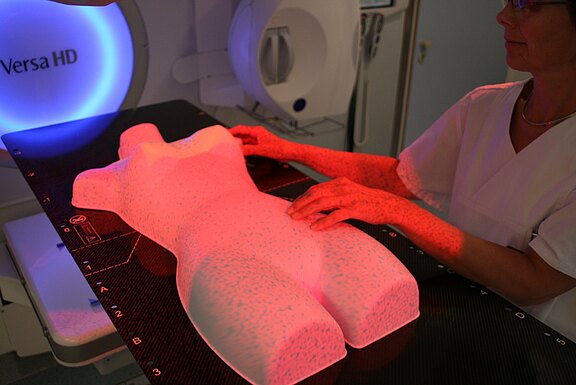 Medizinische Fachkraft richtet einen torsoförmigen Phantomkörper an einem Linearbeschleuniger aus. Rote Laser markieren die korrekte Positionierung zur Strahlentherapie-Kalibrierung.