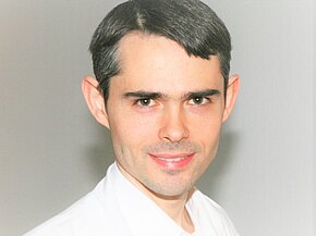 Dr. med. Josef Federhofer Porträtfoto: Nahaufnahme einer lächelnden Person mit kurzen dunklen Haaren, in weißem Hemd vor neutralem Hintergrund.