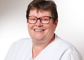 Marion Hahn Porträt einer lächelnden Frau mit großer Brille, kurzen Haaren und weißer Berufsbekleidung vor hellem, neutralem Hintergrund; sie wirkt freundlich und professionell, wie eine Gesundheitsfachkraft.