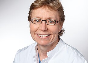 Dr. med. Sonja Braig Porträtfoto: Eine lächelnde erwachsene Person mit Kurzhaar und Brille trägt einen weißen medizinischen Kittel. Frontale Aufnahme vor neutralem Hintergrund, freundlicher Ausdruck, professioneller Eindruck.