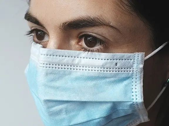 Detailaufnahme eines Menschen mit blauer Einweg-Gesichtsmaske; die Augen sind deutlich sichtbar und blicken seitlich. Motiv steht für Gesundheitsschutz und Infektionsprävention.