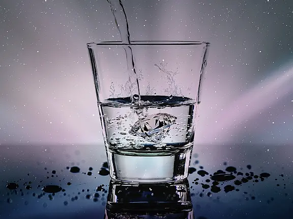 Wasser fließt in ein Glas. Klares Trinkglas, in das Wasser gegossen wird. Ein Diamant im Glas verursacht Spritzer; Tropfen liegen auf der spiegelnden Oberfläche.