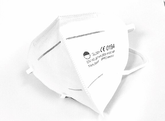 Weiße FFP2-Atemschutzmaske mit Ohrschlaufen in Nahaufnahme. Die Maske zeigt CE-Kennzeichnung und Modellangaben; gefaltetes Design mit Nasenbügel, geeignet zum Schutz vor Aerosolen und Staub.