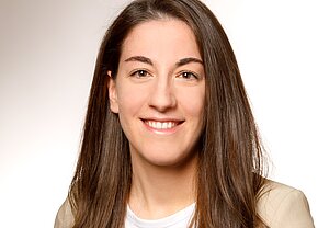 Franziska Bächer Portrait einer lächelnden Frau mit langen, braunen Haaren. Sie trägt ein weißes T-Shirt und einen hellen Blazer. Der Hintergrund ist neutral und hell, wodurch ihr Ausdruck freundlich und einladend wirkt.