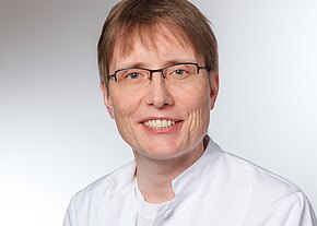 Dr. med. Eva-Maria Babl Ein lächelnder Arzt oder eine Ärztin mit kurzen, braunen Haaren trägt eine weiße medizinische Jacke und Brille. Der Hintergrund ist hell und neutral. Die Person vermittelt einen freundlichen und professionellen Eindruck.