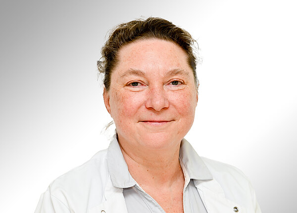 Porträtfoto einer lächelnden Person in weißem Arztkittel vor hellem, neutralem Hintergrund; direkter Blick in die Kamera, freundlicher Ausdruck.