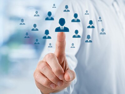 Ein Zeigefinger tippt auf ein zentrales blaues Personensymbol zwischen mehreren Piktogrammen. Darstellung von Auswahl oder Zielgruppen-Ansprache, z. B. Recruiting, Personalmanagement oder Kundenprofilierung.