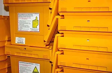 Mehrere stapelbare, orangefarbene Kunststoffbehälter stehen übereinander. Auf jedem Behälter sind Warnhinweise und Gebrauchsanleitungen in deutscher Sprache abgedruckt. Die Behälter sind für die Entsorgung von kontaminierten Materialien vorgesehen.