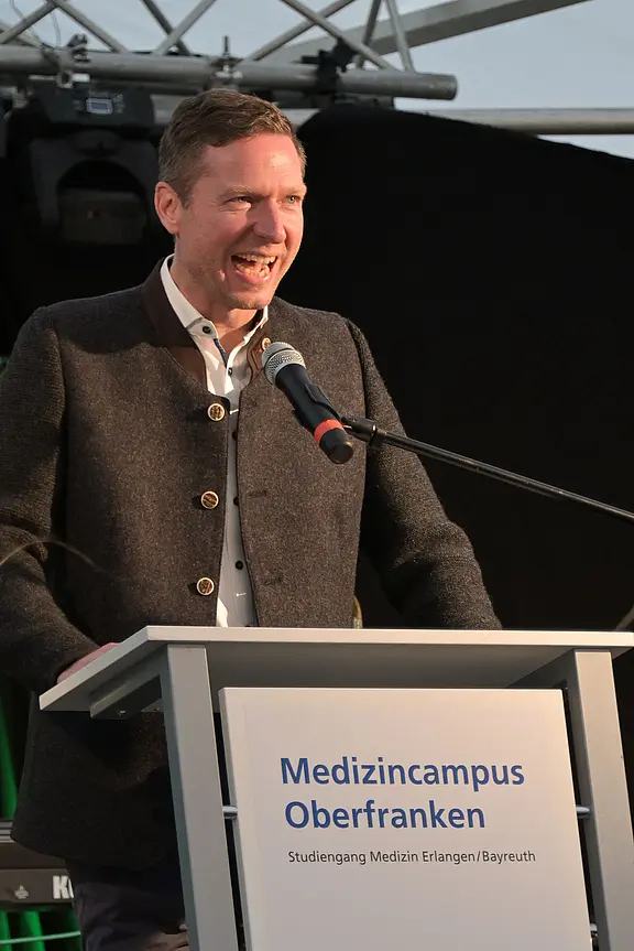 Ein Mann spricht engagiert ins Mikrofon an einem Rednerpult. Auf dem Pult steht: „Medizincampus Oberfranken – Studiengang Medizin Erlangen/Bayreuth.“