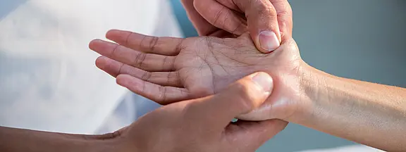 Nahaufnahme: Eine Person hält die geöffnete Hand einer anderen und drückt mit dem Daumen auf den Handballen – Handmassage, Akupressur oder Untersuchung.