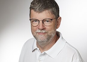 Prof. Dr. med. Rainer Abel Porträt eines Mannes mit grauen Haaren und Brille. Er trägt ein weißes Polo-Shirt und hat einen freundlichen Gesichtsausdruck. Der Hintergrund ist hell und neutral.