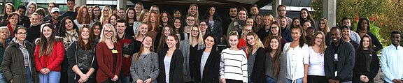 Großes Gruppenfoto: zahlreiche Menschen verschiedener Altersgruppen stehen eng zusammen und lächeln in die Kamera. Die Szene vermittelt Gemeinschaft und Teamgeist.