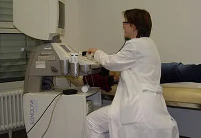 Eine medizinische Fachkraft führt mit einem Ultraschallgerät eine Untersuchung am Bein eines liegenden Patienten durch.