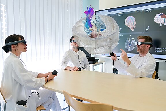OP-Planung: Eine Ärztin, ein Arzt und Prof. Stefan Linsler aus der Klinik für Neurochirurgie blicken durch VR-Brillen auf das raumfüllende Modell eines menschlichen Gehirns.