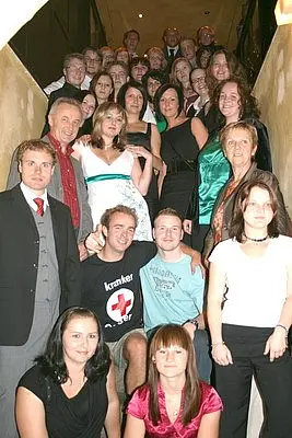 Die Abbildung zeigt eine große Gruppe von Menschen, die auf einer Treppe stehen. Sie sind in verschiedenen Kleidungsstilen gekleidet und lächeln. Die Szene vermittelt ein Gefühl von Zusammengehörigkeit und Feierlichkeit.