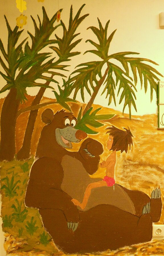 Gemaltes Wandbild: Baloo, der freundliche Bär aus dem Dschungelbuch, sitzt entspannt im Sand und hält den Jungen Mogli lächelnd auf seinem Bauch. Um sie herum stehen Palmen; warme Farben vermitteln tropische, fröhliche Stimmung.