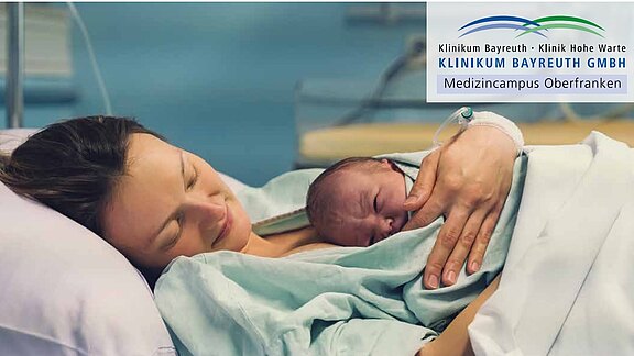 Eine Mutter liegt nach der Geburt im Krankenhausbett und hält ihr neugeborenes Baby eng an der Brust. Beide ruhen im Hautkontakt. Die Szene vermittelt Ruhe, Sicherheit und Geborgenheit.
