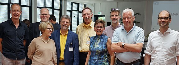 Abschlussmeeting NISCI-Studie Gruppe von neun Erwachsenen steht in einem hellen Konferenzraum, lächelt in die Kamera. Einige tragen Namensschilder; Kleidung ist business-casual. Stimmung freundlich, wirkt wie ein Workshop oder Netzwerktreffen.