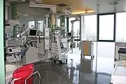 Heller, leerer Intensivstationsraum im Krankenhaus mit modernen Monitoren, Beatmungsgeräten und medizinischen Gerätearmen; aufgeräumt, große Fenster lassen Tageslicht hinein.