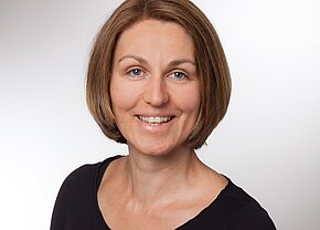 Christine Degelmann Porträt einer lächelnden Frau mit kurzen, braunen Haaren. Sie trägt ein schwarzes Oberteil und steht vor einem hellen Hintergrund. Die Frau hat ein freundliches und offenes Ausdruck, das eine positive Atmosphäre vermittelt.