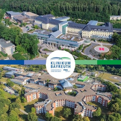 Luftaufnahme des Klinikum Bayreuth, die zwei Gebäudeansichten in einem grünen Umfeld zeigt. Im oberen Bereich ist ein modernes Gebäude zu sehen, während im unteren Bereich eine weitere Institution des Klinikums abgebildet ist, darunter das Logo „Klinikum Bayreuth“.