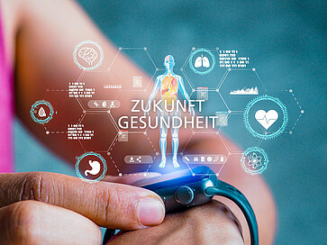 Eine Person überprüft ein tragbares Gesundheitsgerät am Handgelenk. Über dem Gerät schwebende grafische Symbole zeigen Gesundheitsdaten, einschließlich einer menschlichen Silhouette mit hervorgehobenen Organen und verschiedenen Gesundheitsindikatoren. Der Text „Zukunft Gesundheit“ ist deutlich sichtbar.